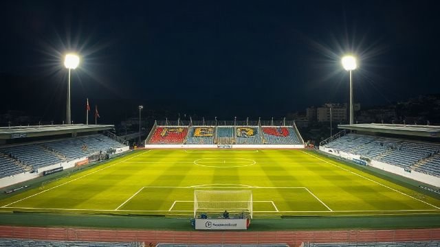 A football stadium at night with bright floodlights and empty stands.